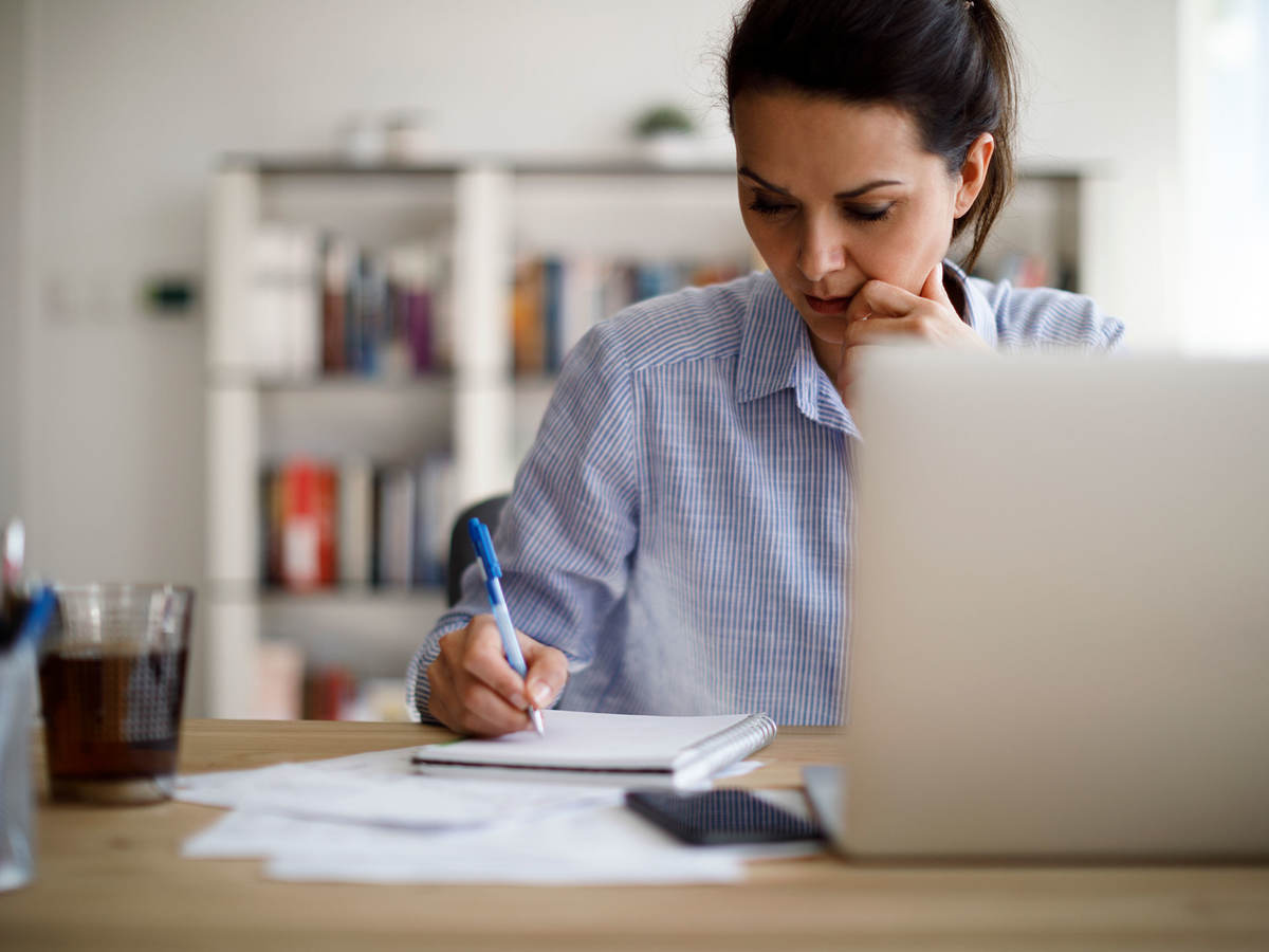 Person writing something down while working on a laptop