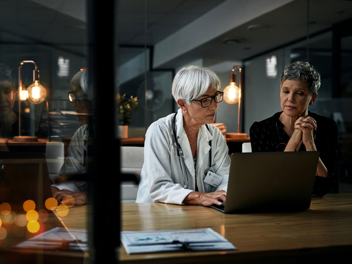 Two medical professionals reviewing notes on a laptop