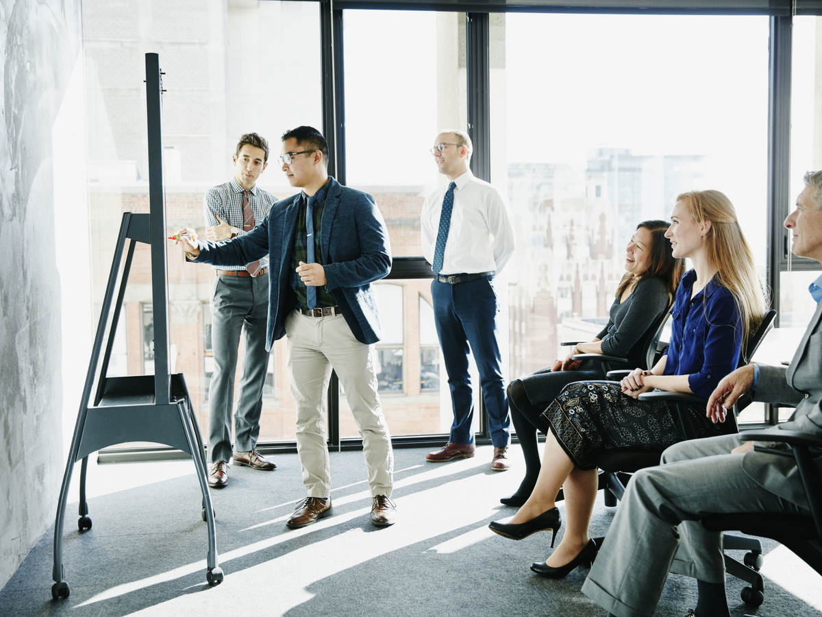 Group of colleagues having a meeting while one presents on a board