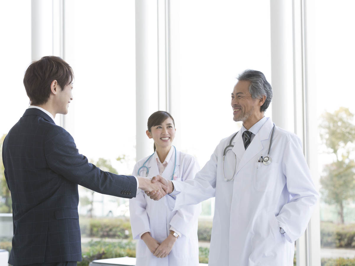 Person in a suit greeting two doctors
