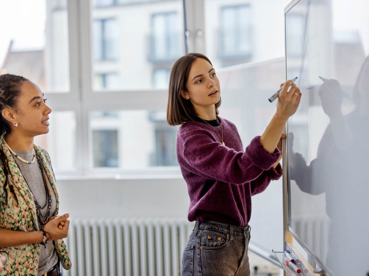 Two business colleagues collaborating while one writes on a whiteboard