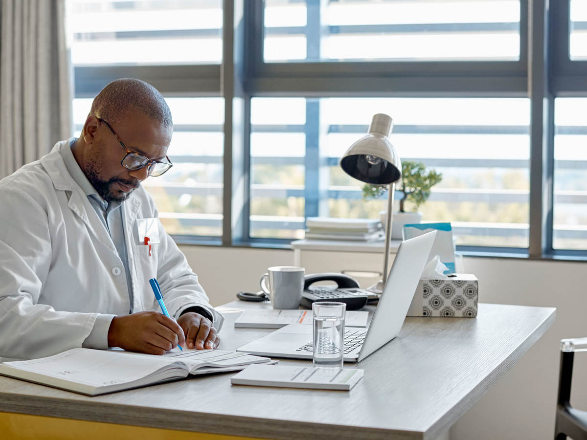 Doctor taking notes while taking an online class in an office