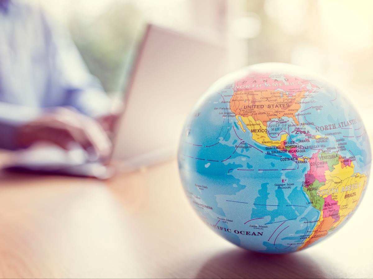 Globe sitting on a desk while someone uses a laptop in the background