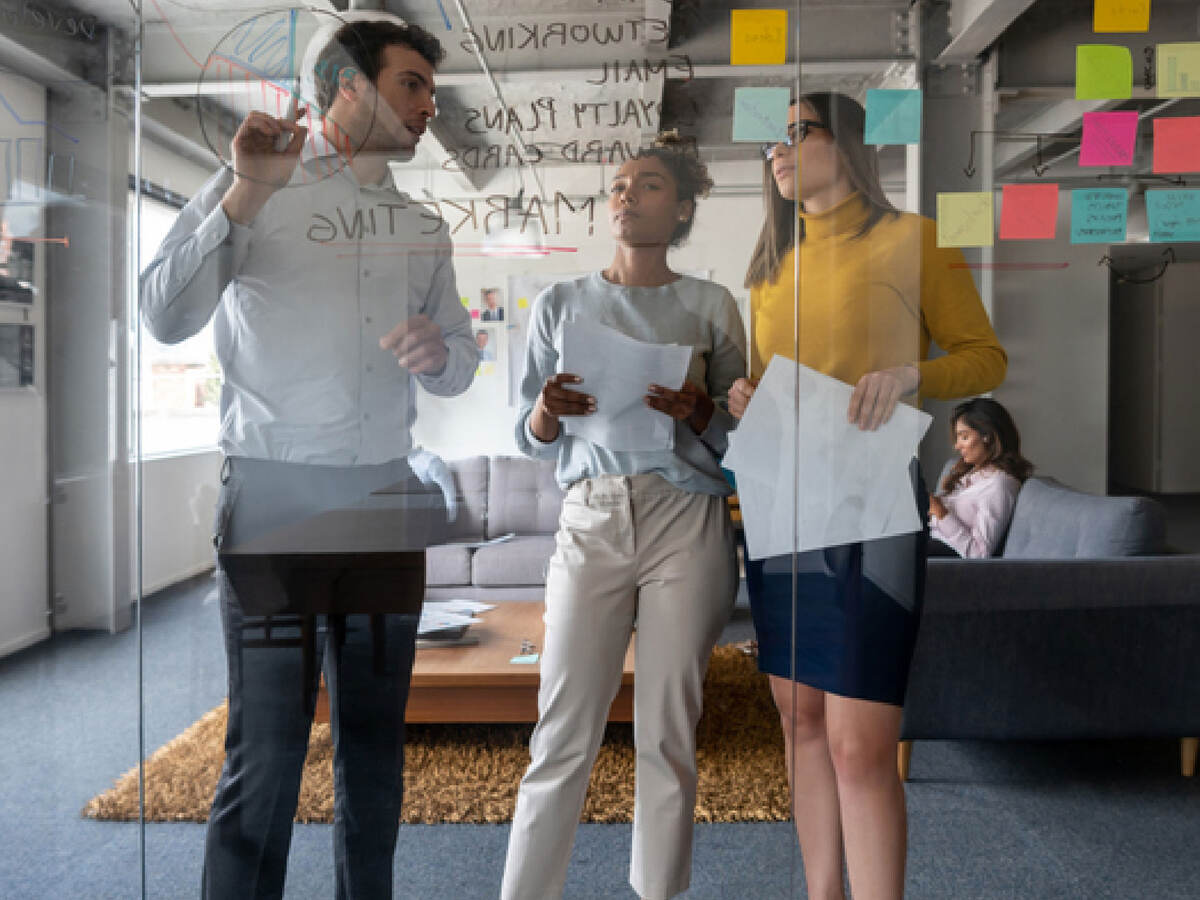Three coworkers collaborating together in front of a glass wall