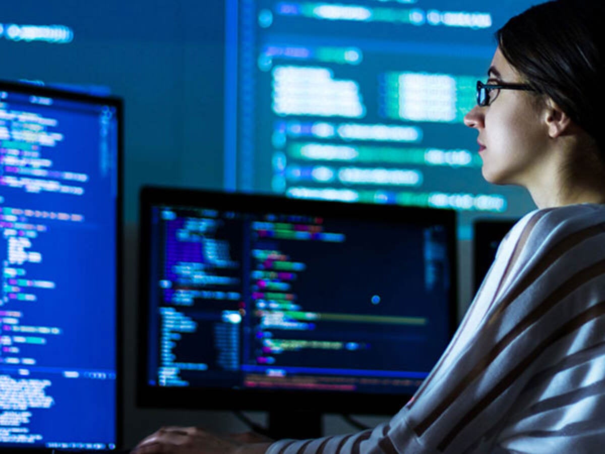 Person sitting in front of giant monitors while coding in a dark room