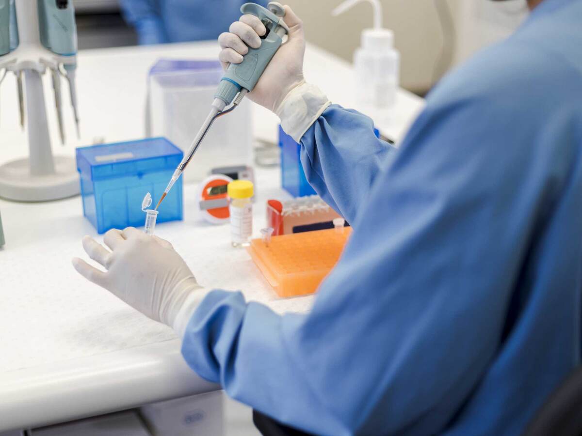 Scientist using a pipet while holding a vial