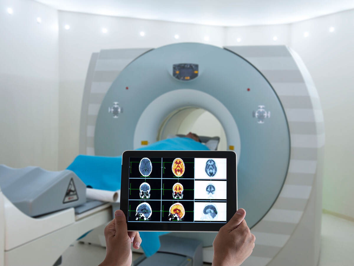 Doctor viewing an MRI on a tablet while standing in front of the patient laying inside the MRI