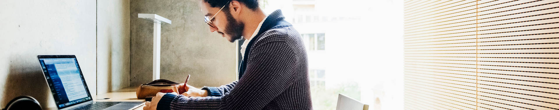 Person sitting at desk using a laptop and taking notes