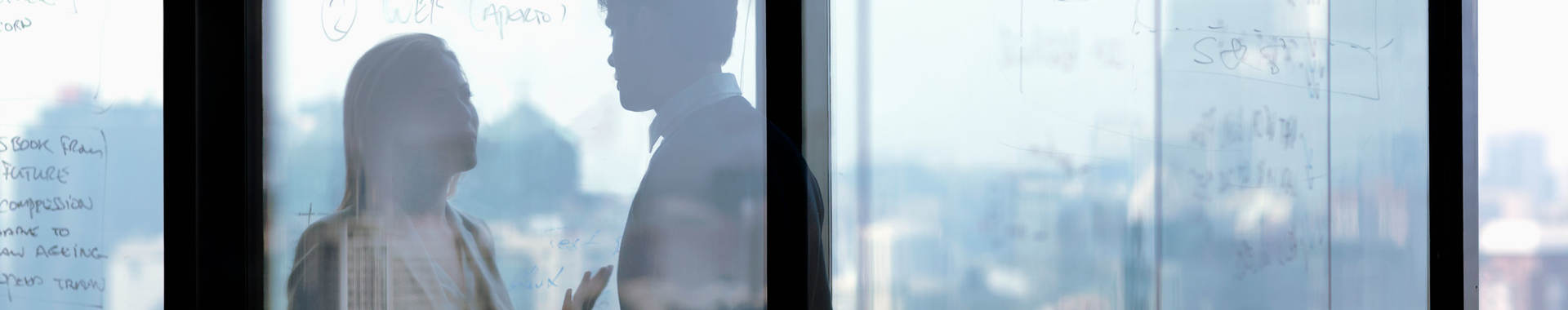 Two coworkers speaking in a glass conference room