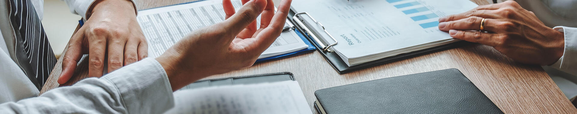 People with notebooks at a desk having a conversation