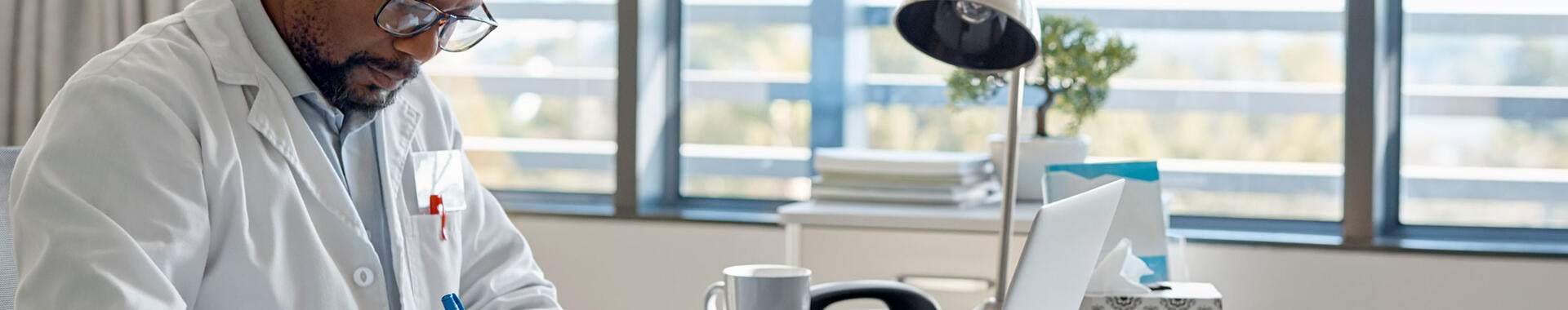 Doctor taking notes while taking an online class in an office