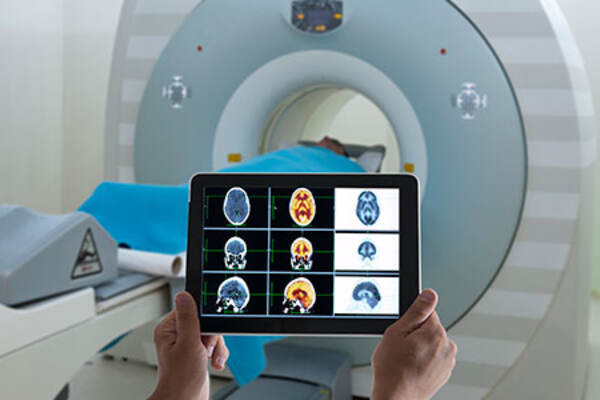 Doctor viewing an MRI on a tablet while standing in front of the patient laying inside the MRI