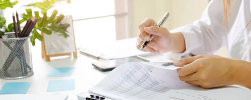 Person sitting at desk reviewing documents with a pen