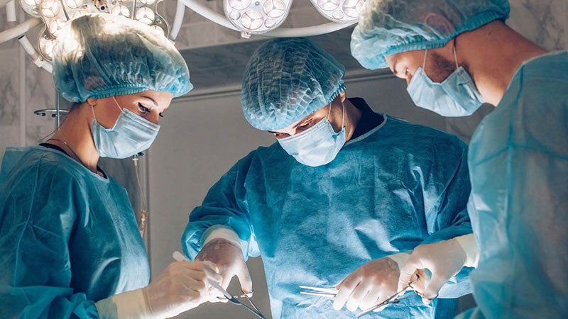 Three surgeons stitching up a patient