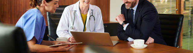 Three people sitting around a desk smiling and looking at a laptop