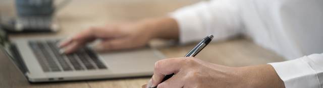Person working at a laptop while checking a clipboard.