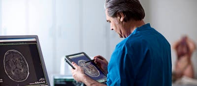 Doctor holding portable computer. Looking at MR scan image of human brain on screen