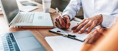 Person working on a desk and taking notes on a clipboard