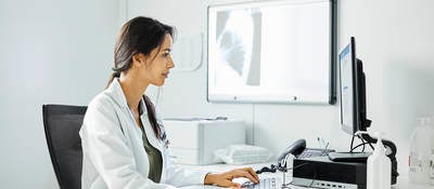 Confident doctor using computer at desk. Female medical professional is working in clinic. She is wearing lab coat.