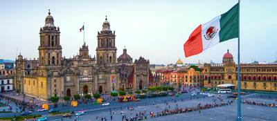 The Mexican flag flies over the Zocalo, the main square in Mexico City. The Metropolitan Cathedral faces the square, also referred to as Constitution Square.