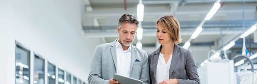 Two people walking through a factory looking at a tablet