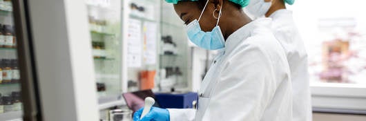 Two scientists making medicine at a laboratory. Doctors working together at pharmacy lab wearing protective work wear.