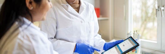 Lab technician smiling and pointing to a tablet