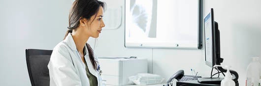 Confident doctor using computer at desk. Female medical professional is working in clinic. She is wearing lab coat.