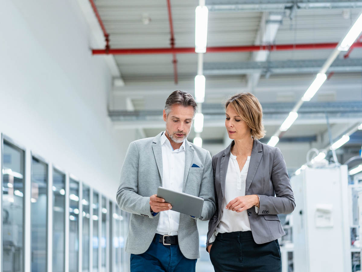 Two people walking through a factory looking at a tablet