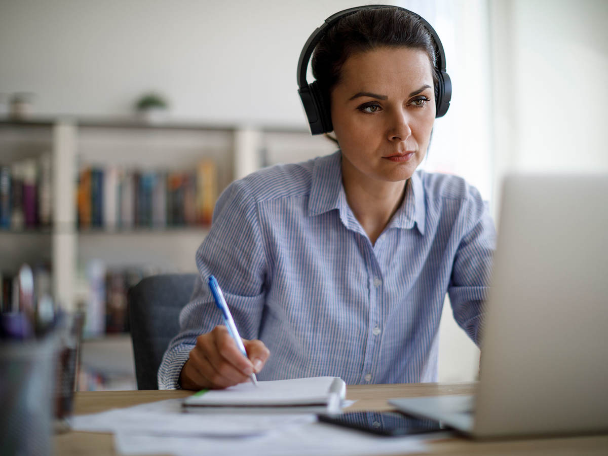 Woman with headphones making notes while looking at a laptop